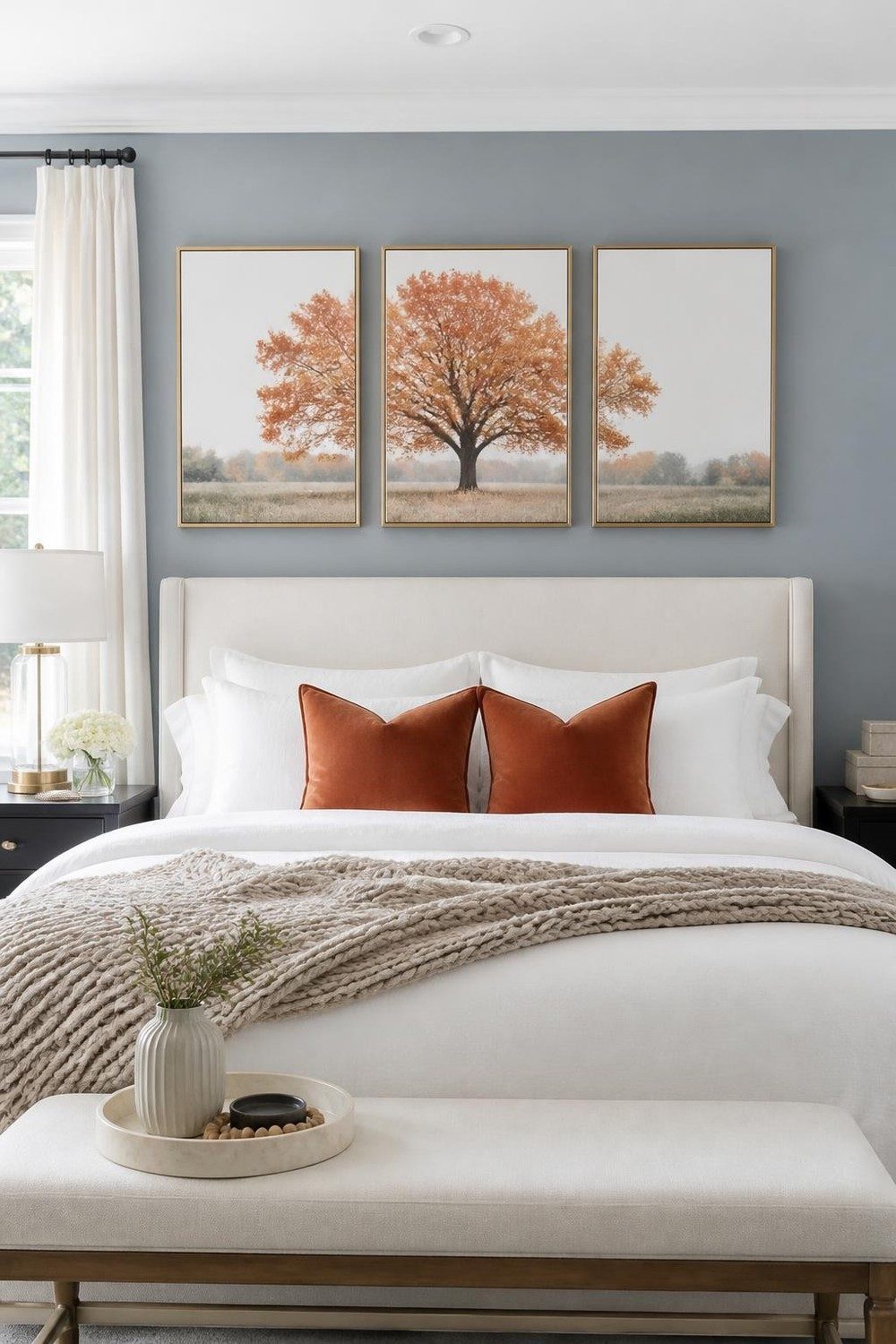 Three brass-framed autumn tree prints above a cream headboard on a dusty blue bedroom wall